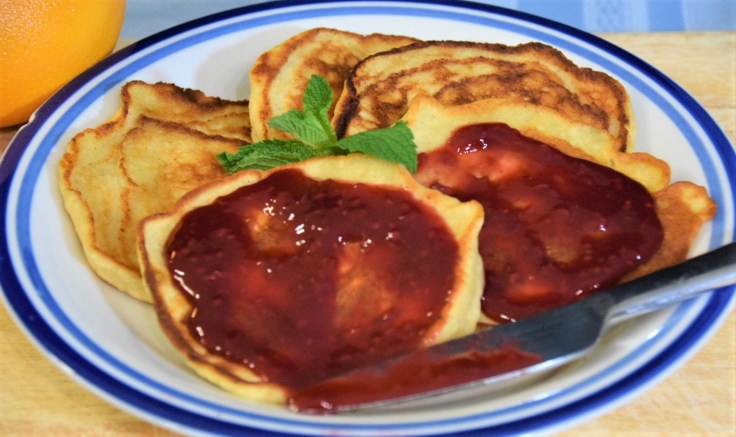 Small stack of cheese pancakes topped with fruit preserves and garnished with mint on a plate