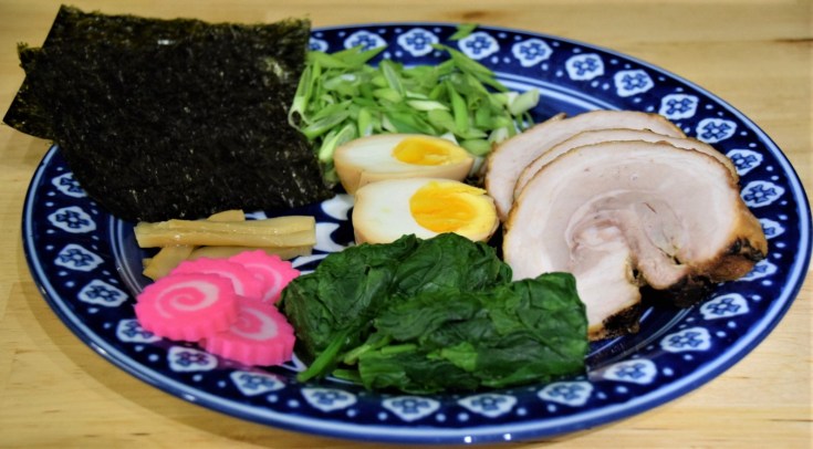 ramen toppings on a blue and white plate menma chashu pork egg ajitsuke tamago scallions nori menma narutomaki kamaboko spinach