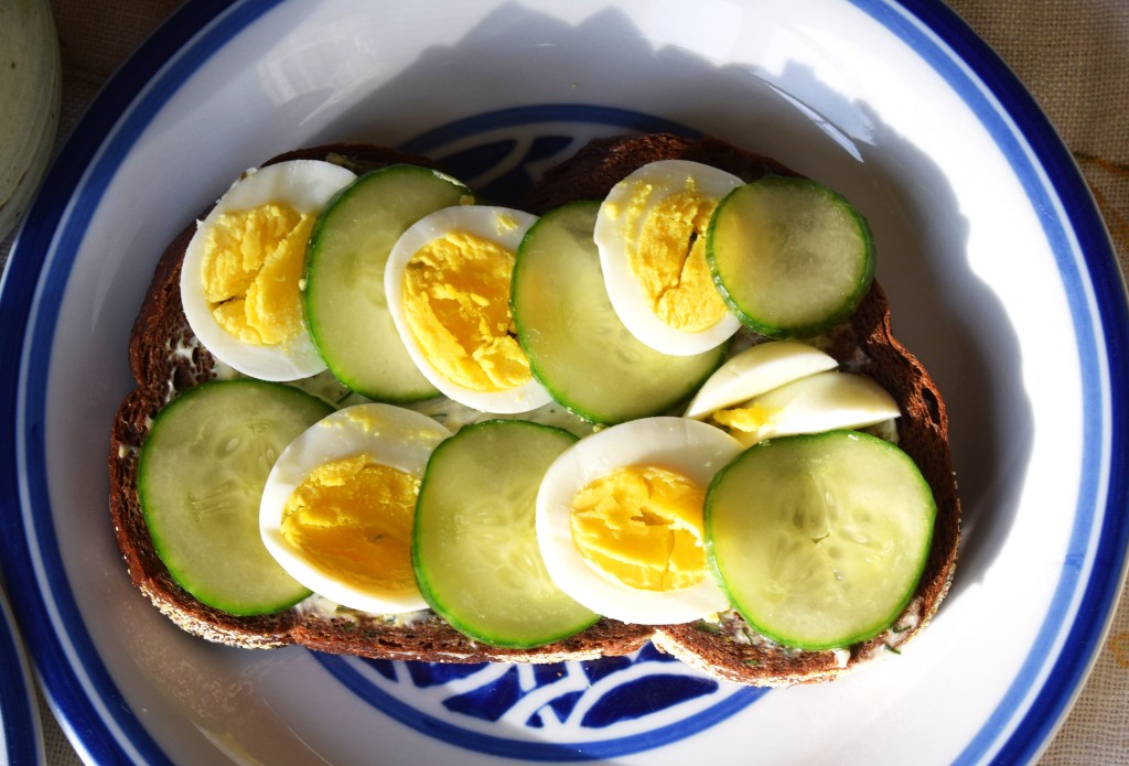An open-faced cucumber and boiled egg sandwich on a blue and white plate.